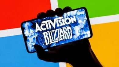 Pessoa segurando celular com imagem da logomarca da Activision na tela e, ao fundo, logomarca do Windows, da Microsoft
