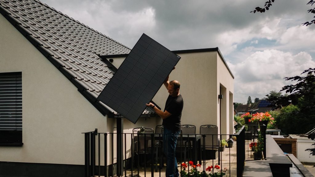 Imagem de Patrick Junker instalando um painel solar pequeno no telhado de uma casa