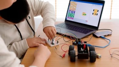 Jovens mexendo em fios de carrinho conectados a notebook durante aula de robótica